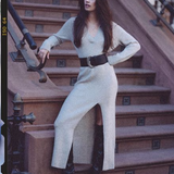 A woman wearing a light beige knit long-sleeve dress with a high slit and a wide black belt, posing on outdoor stone steps.
